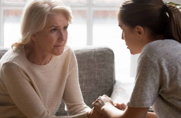 Erwachsene Tochter hält die Hände ihrer älteren Mutter, um sie in einem sensiblen Gespräch über Pflege und Unterstützung zu trösten und zu begleiten